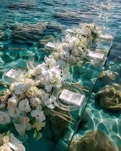 the table is set up with flowers and place settings for an outdoor wedding ceremony in clear water