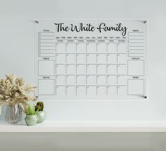 the white family wall calendar is on display next to two vases with flowers in them