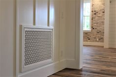 an air vent in the corner of a room with wood floors and white walls, next to a brick wall