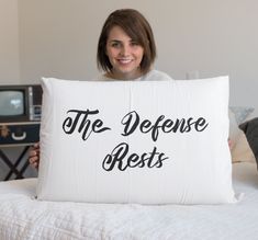 a woman holding a pillow that says the defense rests on it in front of her