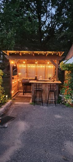 an outdoor bar is lit up at night with lights on the roof and barstools