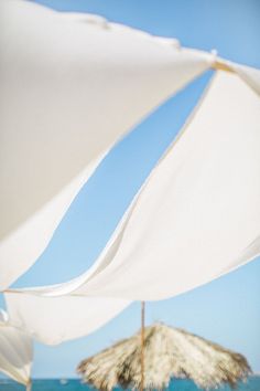 two umbrellas on the beach with clear blue water in the background and people sitting under them