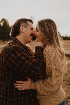 a man and woman standing together in the middle of an open field with their hands around each other