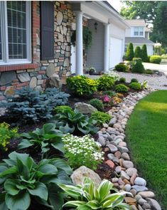 a garden with rocks and flowers in front of a house