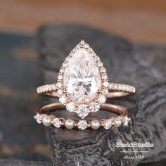 an engagement ring set with a pear shaped diamond and pearls on the side, sitting on top of a rock