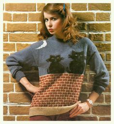 a woman standing in front of a brick wall wearing a sweater with cats on it