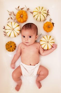 a baby laying in a bathtub surrounded by pumpkins