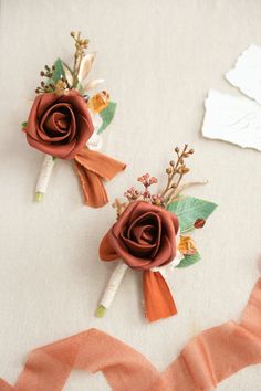 two boutonnieres with flowers on them sitting on top of a white table cloth