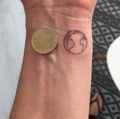 a small tattoo on the wrist of a person with a coin in front of it