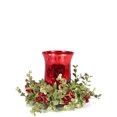 a red glass vase sitting on top of a table next to green leaves and berries