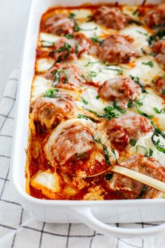 a casserole dish with meatballs, cheese and spinach in it on a towel