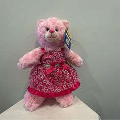 a pink teddy bear wearing a dress on top of a white tablecloth covered pedestal