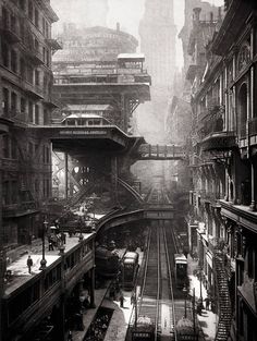 an old black and white photo of trains on tracks in a city with tall buildings