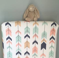 a teddy bear sitting on top of a pillow with arrows in the back and an arrow pattern