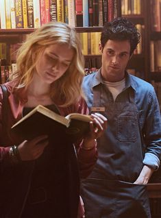 a man and woman standing in front of a bookshelf with an open book