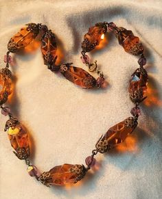 I just love brass and glass necklaces. They are so ornate and really lovely. This one is 17 inches long. The orangey gold glass beads ae 1 inch long by just under 1/2 inch wide. They are capped by filigree brass caps and interspaced with purple beads. The orange beads are cut like cubist style, very art deco. C. 1930 and Czech. Follow me on instagram@jettesjewels. Vintage Bronze Beaded Necklace With Large Beads, Vintage Bronze Beaded Necklaces With Large Beads, Vintage Czech Glass Necklace With Faceted Beads, Vintage Brass Necklace With Round Beads, Vintage Czech Glass Polished Beads Necklace, Vintage Czech Glass Necklace With Polished Beads, Vintage Czech Glass Necklaces With Polished Beads, Vintage Brass Beaded Necklace With Round Beads, Vintage Bronze Beaded Brass Necklaces