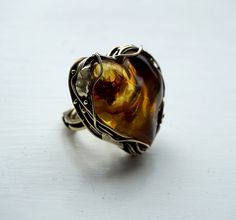 Magnificent heart ring with natural amber. The stone is absolutely natural, unrefined, the age of the stone is 45 million years. There is a natural beautiful pattern inside the stone, every time you look at it you can find something new inside. The frame is made entirely by hand from jewelry brass. The ring is adjustable in size. Description: Size of the topper with stone-1.4*1.43 inches  Weight 21.66 g We pack ring the in a wooden box. Delivery: The parcel will be sent during 2-3 days after pay Handmade Adjustable Baltic Amber Jewelry, Unique Baltic Amber Jewelry For Gifts, Handmade Baltic Amber Jewelry, Handmade Baltic Amber Ring, Unique Amber Wedding Rings, Baltic Amber Ring Jewelry Gift, Handmade Adjustable Citrine Rings, Unique Adjustable Heart-shaped Ring, Unique Adjustable Heart Shaped Ring