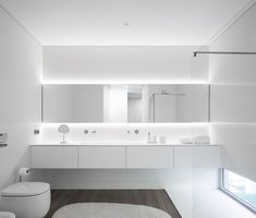 a white bathroom with two toilets and a large mirror