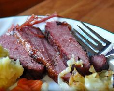 a white plate topped with meat and potatoes on top of a wooden table next to a fork