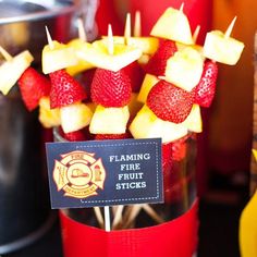 strawberries and apples are arranged on sticks in a clear glass vase with a fireman's name tag