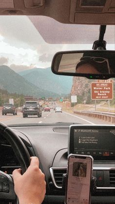 a person is using their cell phone while driving down the road with mountains in the background