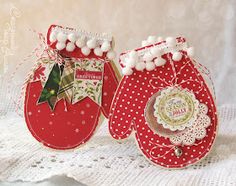 two red mittens with white pom poms are sitting on a lace doily