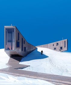 a man walking up the side of a snow covered slope next to a tall building