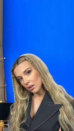 a woman with long blonde hair sitting in front of a blue background