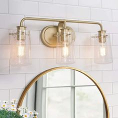 a bathroom vanity light with three lights and a round mirror on the wall above it