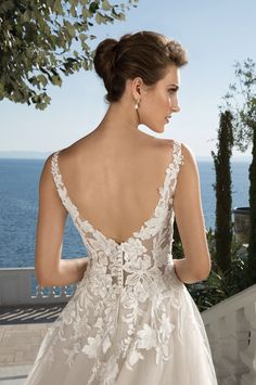 a woman in a wedding dress looking out at the ocean from behind her is an open back view