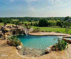 an outdoor swimming pool with waterfall and rock walls, surrounded by lush greenery on the other side