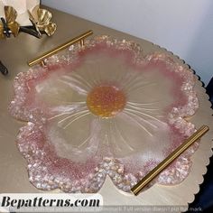 a pink glass dish sitting on top of a table next to two gold hair pins