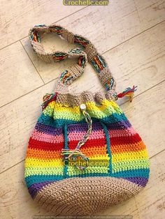 a multicolored crocheted bag sitting on top of a wooden floor next to a purse