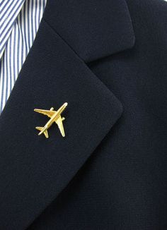 a gold airplane pin sitting on top of a black suit jacket with a striped shirt underneath