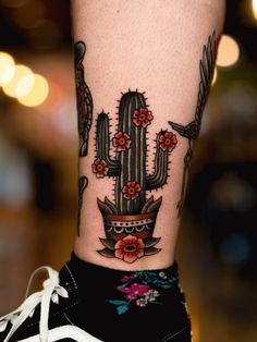 a tattoo on the leg of a person with a cactus and flower arrangement in it