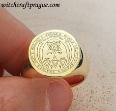 a gold ring with the seal of solomon written on it, in front of a person's finger