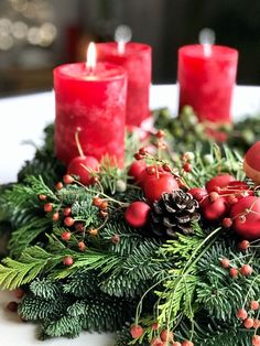 a table topped with red candles and greenery covered in pine cones, berries and holly