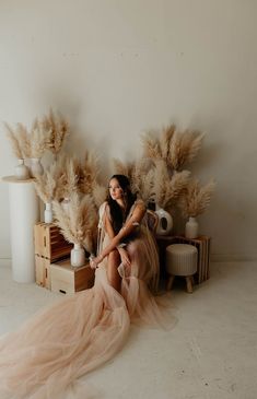 a woman sitting on top of a wooden box next to tall dry grass and vases