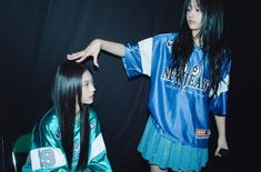 two young women standing next to each other in front of a black background, one wearing a blue and white shirt