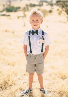 a young boy wearing a bow tie and suspenders standing in the middle of a field