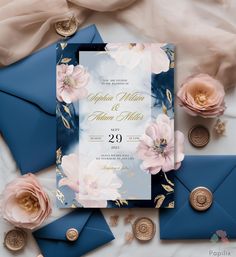 an elegant wedding suite with blue envelopes and pink flowers on the front, along with gold accents