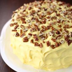 a cake with white frosting and pecans on top sits on a plate, ready to be eaten