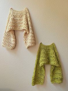 two crocheted sweaters hanging on the wall next to each other, one is green and the other is white