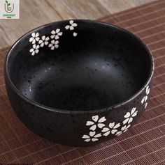 a black bowl with white flowers painted on the side sitting on a brown place mat