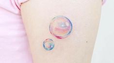 two soap bubbles on the side of a woman's thigh, one is pink and blue