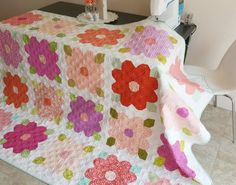 a table with a quilt on it that has flowers on it and a white chair next to it