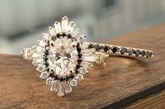 an engagement ring with black and white stones on it sitting on top of a wooden table