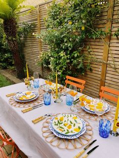 a table set with plates, glasses and utensils in front of a fence