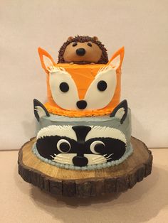 three tiered cake decorated to look like animals with faces on each layer, sitting on top of a tree stump