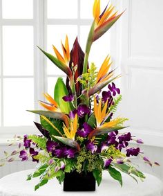 an arrangement of flowers on a table in front of a white wall and windowsill